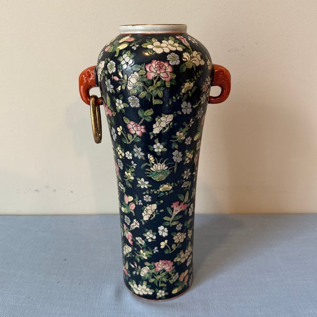 Vintage Asian style Famille Noir vase with lots of flowers, orange handles, and a gold ring hanging off one handle.