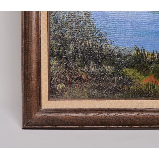 The framed painting depicts a serene landscape with a body of water, likely a lake or river, and a small rowboat pulled up...