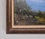 The framed painting depicts a serene landscape with a body of water, likely a lake or river, and a small rowboat pulled up...