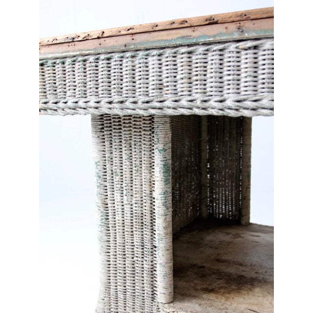 A lovely antique wicker library table featuring a wood top and lower shelf. The woven wicker base retains its original...