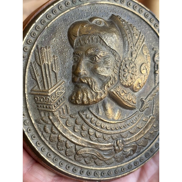 Antique cast bronze plaque mounted to leather with felted bottom, for tabletop display. It features a Neoclassical style...