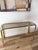 Elegant vintage Hollywood Regency console table featuring a polished brass frame with waterfall edges and inset smoked...