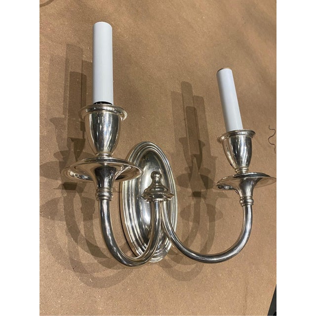 A classic double-arm wall sconce with a polished metal finish. Oval-shaped backplate with layered contours, adding a...