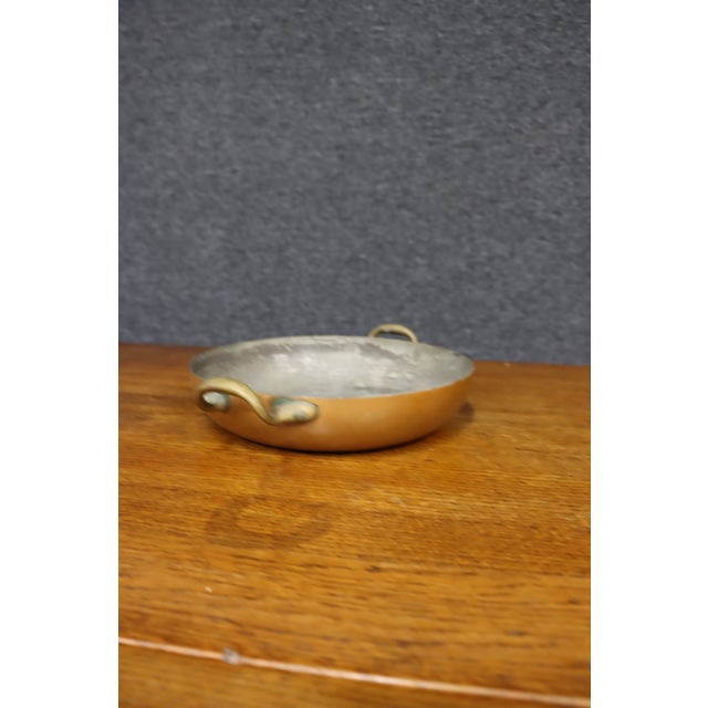 Antique shallow copper cooking pan with a rounded form, two applied brass loop handles, and a traditional tinned interior....