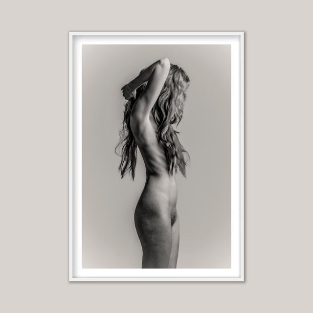 A black-and-white photograph of a nude young woman, her elegance heightened by the obscuring veil of long, tousled hair....