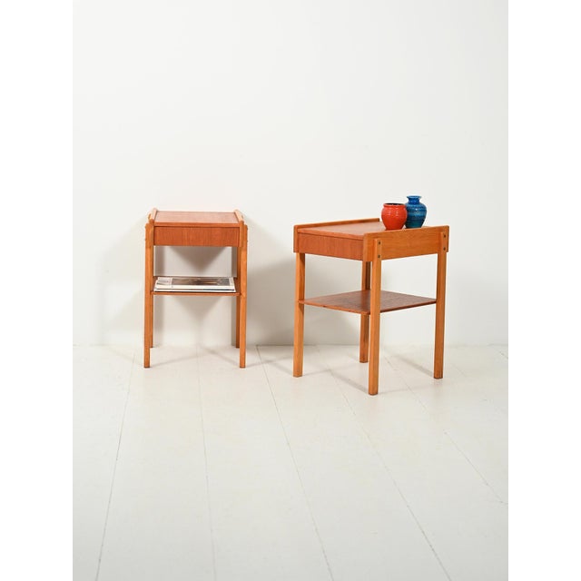 A pair of 1960s Scandinavian teak bedside tables with an orthogonal profile: a concealed drawer, a magazine rack, and...
