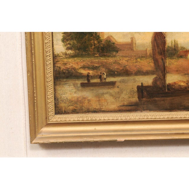 A European riverside village landscape oil painting, in gilt frame, from the 19th century. This antique painting from...