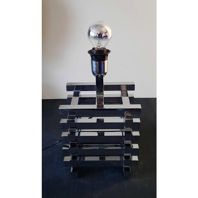 This table lamp has a modern and elegant design, characterized by a geometric structure with overlapping lines in chromed...