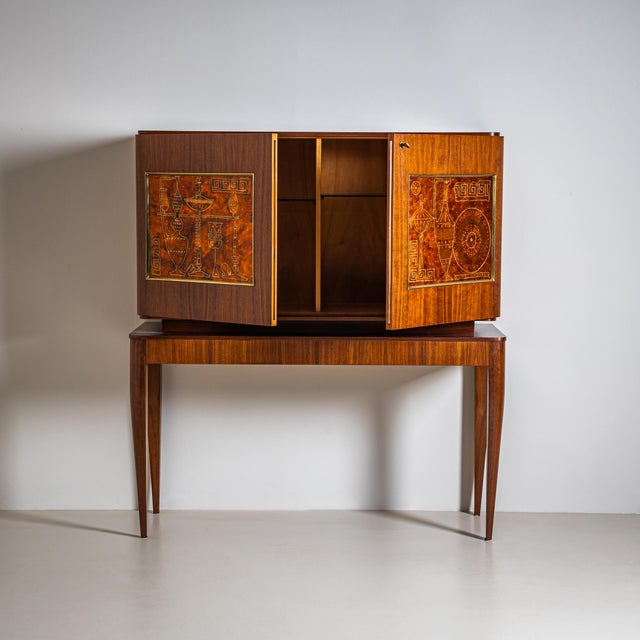 Two-door wooden bar cabinet on tall tapered legs with recessed panels, decorated with antique amphora motifs and meander...