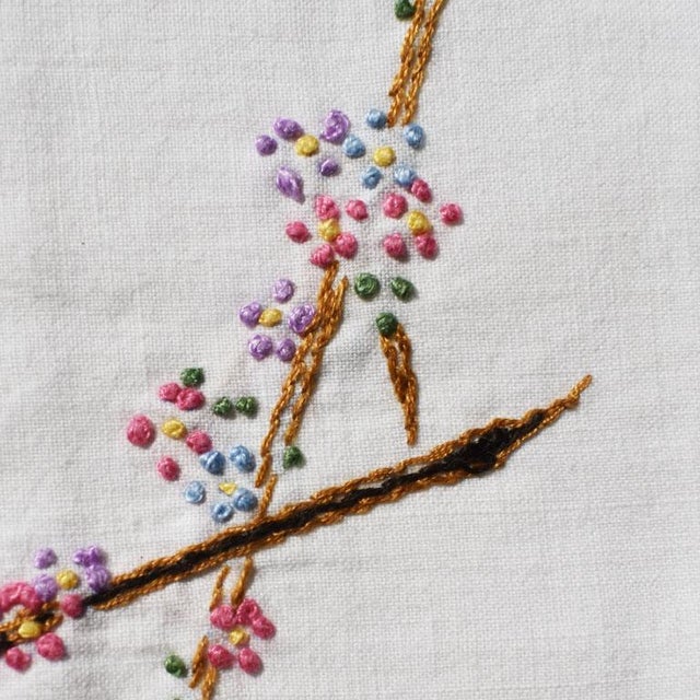 A set of four cream table napkins with a hand-stitched chinoiserie floral motif. Each napkin is in cream, with a hand-...