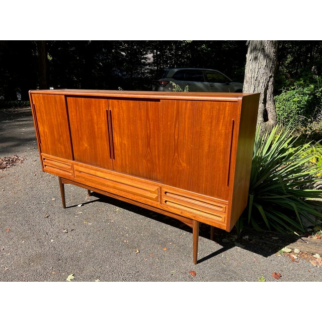 Designed by Johannes Andersen, this Danish modern teak highboard is a beautiful example of Scandinavian craftsmanship with...