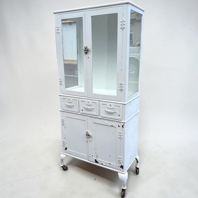 A vintage metal painted medical cabinet. An unusual form having 2 doors above 3 drawers above 2 more doors again for more...