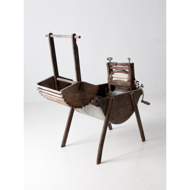 This is an antique washing machine circa late 19th century. The wooden frame wash stand features a galvanized metal tub...