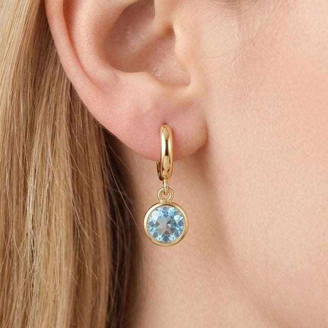These elegant drop earrings feature radiant Blue Topaz gemstones, beautifully suspended from sleek gold hoops for a...