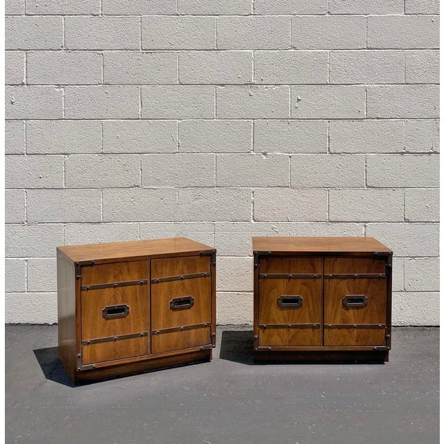 A pair of 1970s vintage campaign nightstands in patina brass and wood veneer. Nightstands are in good condition and...