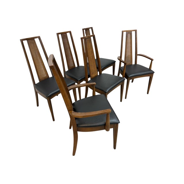 Elevate your dining space with this stylish set of six circa 1970s walnut dining chairs featuring elegant cane backs....