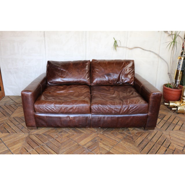 A beautifully aged two-seat leather sofa by Restoration Hardware, offering timeless design, exceptional comfort, and a...