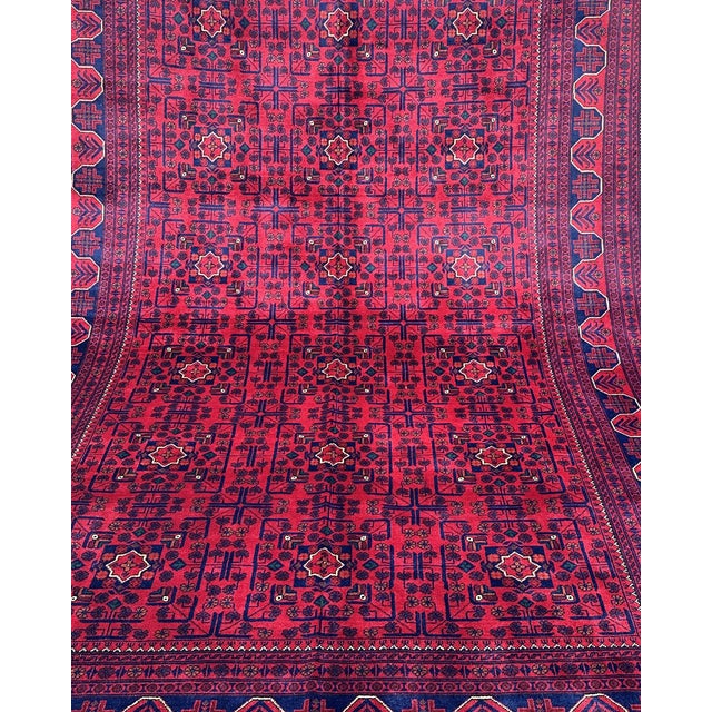 A richly saturated crimson field is covered in precise, repeating gul medallions — the hallmark motif of the Khal...