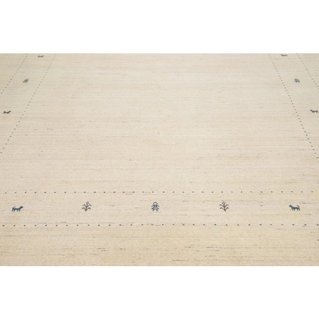 The contemporary appeal of this woolen rug, in the style of Gabbeh, lies in its minimalistic beige pattern and gray color...