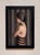The artwork depicts a figure in profile, subtly shying away, enveloped in a muted palette of grays and earth tones....