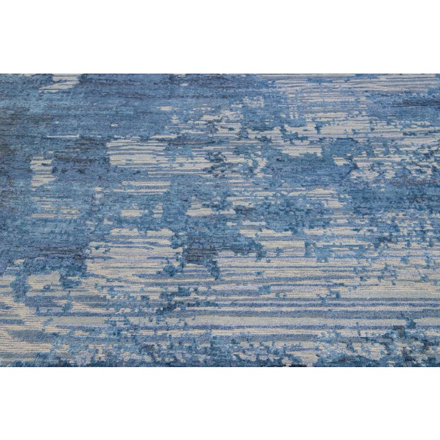 This Indian wool and silk blend rug features a gray field with an abstract pattern detailing blue satin. Its composed...