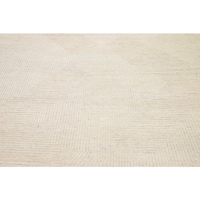 The wool rug, crafted with the hand-knotting technique, features a contemporary design inspired by Moroccan motifs. Its...