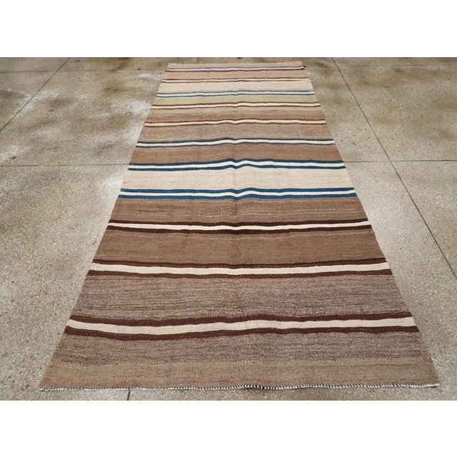 This Mid-20th century Persian Flatweave Kilim gallery runner, features a harmonious blend of earthy tones and bold...