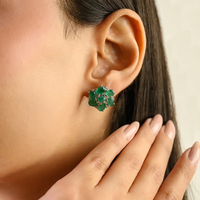 A striking pair of vintage emerald and diamond cluster earrings crafted in silver, showcasing a total gemstone weight of...