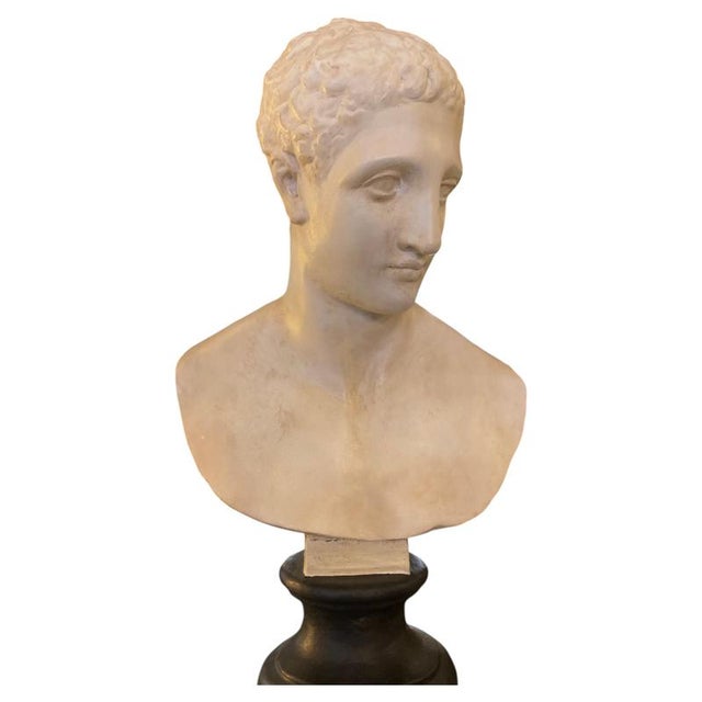 The subject is a bust of the god Hermes, made in the early 1900s from white plaster with a matte finish and sculpted...