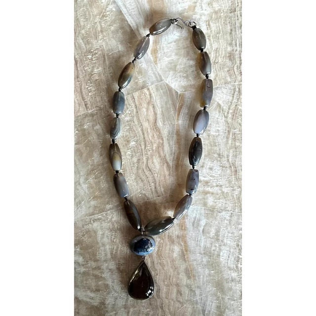This vintage necklace is a bold, earthy strand of large, polished agate beads in a quiet palette of smoky gray, taupe,...