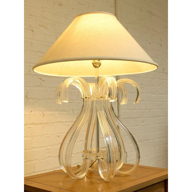 A glamorous sculptural table lamp featuring a clear lucite base formed from sweeping loops and curved lucite ribbons...