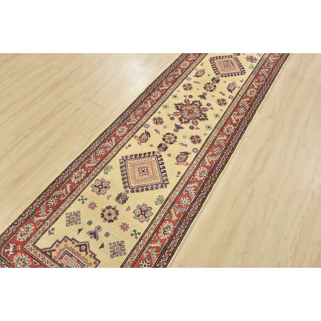 A tribal Caucasian Kazak runner hand-knotted with an all-wool pile on a cotton foundation. This oriental rug features...