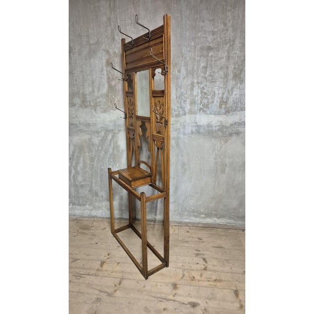 A striking vintage hall tree made of carved oak, featuring an integrated central mirror, multiple coat hooks, decorative...