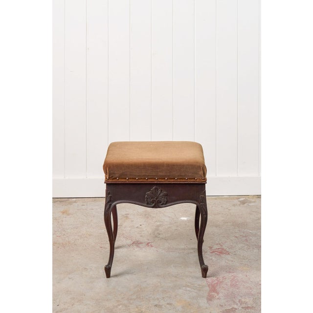 This carved piano stool features bronze velvet upholstery and brass nailhead trim over carved shell motifs in the dark...