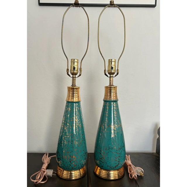 A pair of vintage mid-century modern ceramic table lamps featuring a distinctive turquoise or teal glaze with gold...