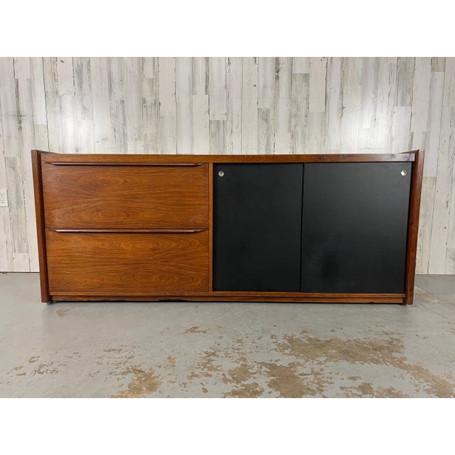 Classic figural rosewood Danish Modern credenza with black masonite sliding doors. There is a shelf behind the sliding...