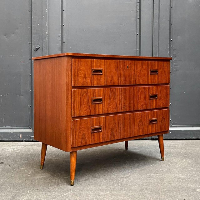 Product: chest of drawers style: mid-century · 1960s material: teak veneer · partially solid wood · brass feet features:...