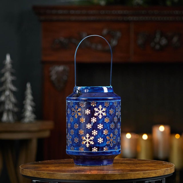 Bring the cozy charm of winter indoors with this 9.5" snowflake punched metal candle lantern. Finished in a rich navy blue...