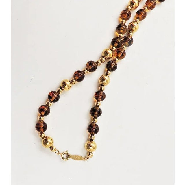 This is part of Chairish’s Costume Jewelry assortment. 1980s goldtone and faux-tiger's eye beaded necklace with spring...