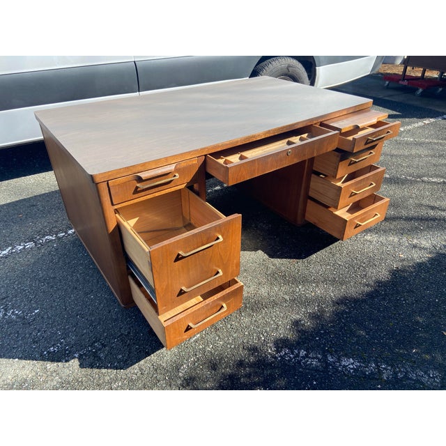 The Vintage Mid Century Modern Jofco Walnut Tanker Desk is a stylish and unique piece of office furniture that exudes a...