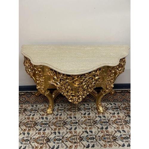 A beautifully crafted giltwood console table featuring an intricately carved apron with scrolling foliage details. The...