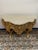 A beautifully crafted giltwood console table featuring an intricately carved apron with scrolling foliage details. The...