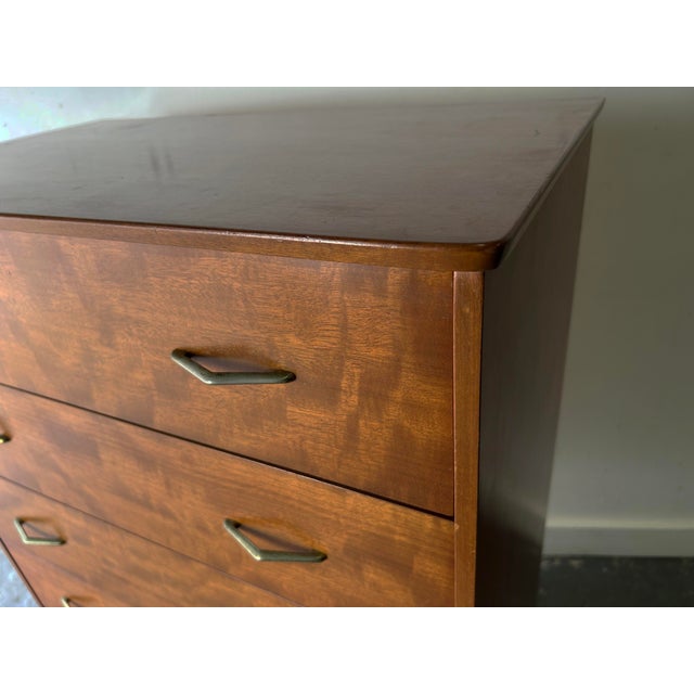 A handsome mid-century chest of drawers in warm walnut veneer, standing on slender tapered splayed legs with metal tips....