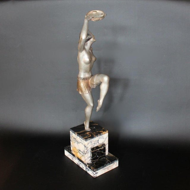 An Art Deco, cold painted spelter sculpture of a dancer with a tambourine in hand, set over a stepped, bi-coloured marble...