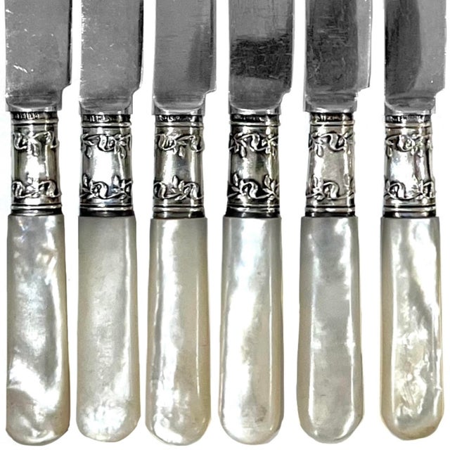 This set of six early 20th century fruit or desert knives feature mother-of-pearl handles, sterling silver ferrules, and...