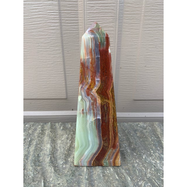 A beautifully proportioned marble obelisk in richly veined shades of green, brown, cream, and tan. The sculptural...