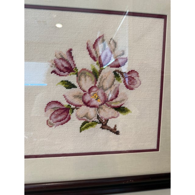 This framed artwork features a completed cross-stitch embroidery piece showcasing a delicate magnolia flower branch. The...