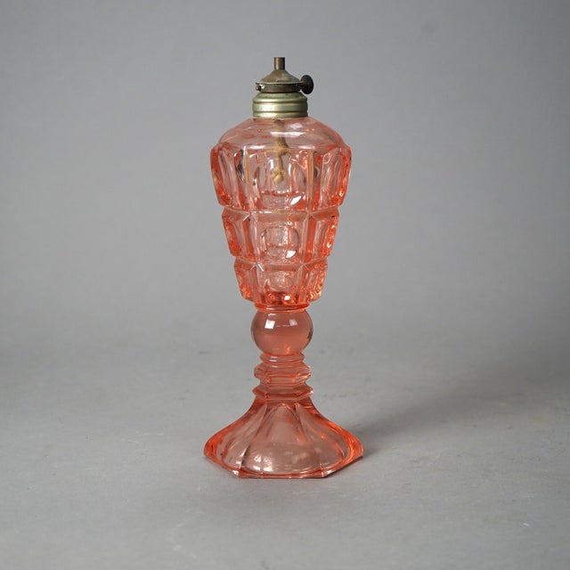 An antique oil lamp offers pink pressed glass construction with paneled coinspot pattern raised on column with hexagonal...