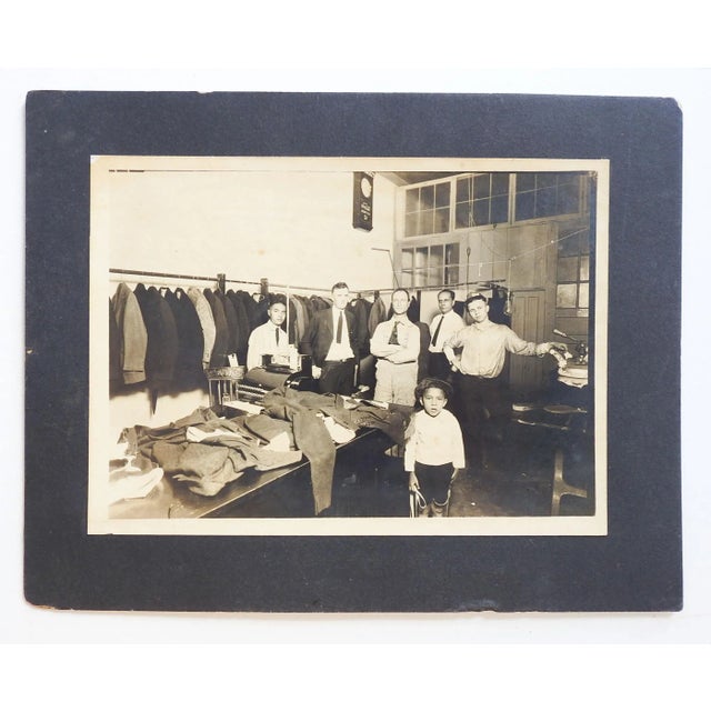 Vintage photograph of the interior of a tailor shop mounted on black cardboard. Workers, including child, Coca Cola clock....