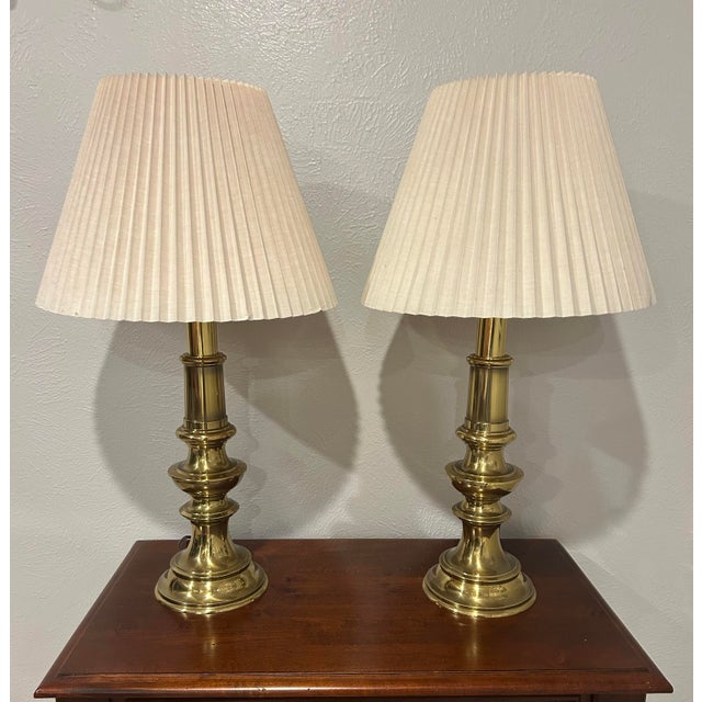 Classic pair of Stiffel brass candlestick-style table lamps with tiered column bases and original cream pleated fabric...